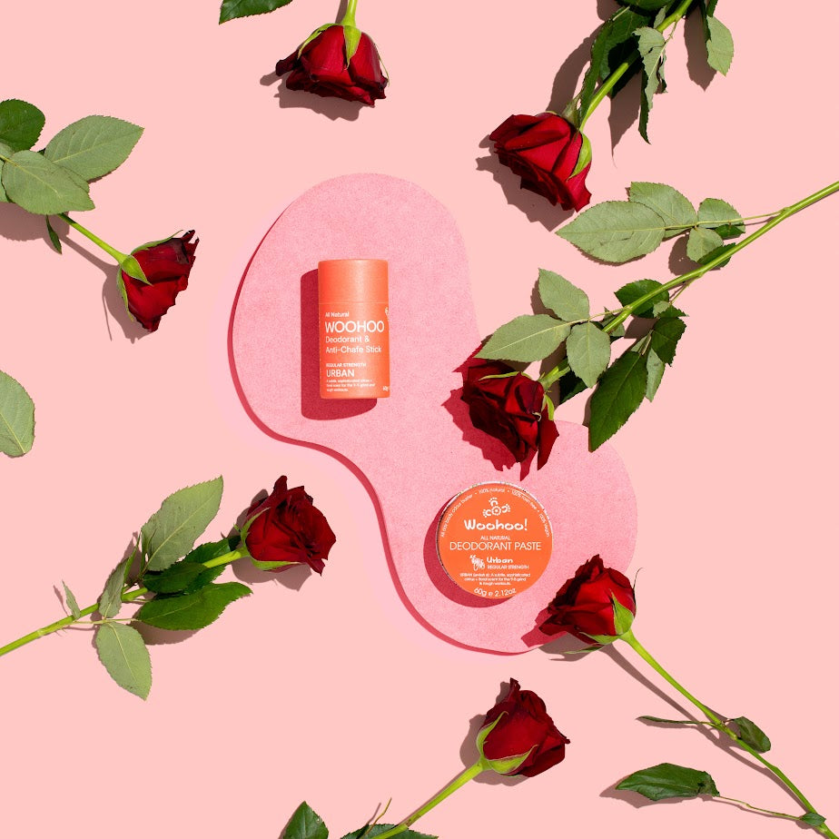 Image of Urban Natural Deodorant Stick and paste on a pink platform surrounded by roses to highlight the rose scent and rose oil essential ingredient on a pink background