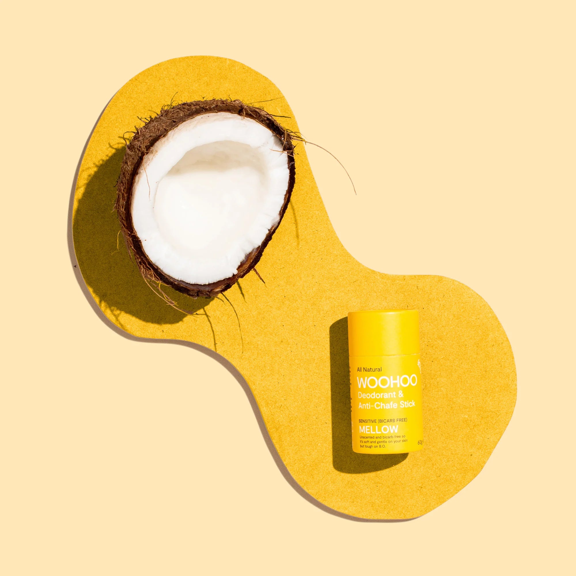 Image of Mellow Natural Bicarb-free Deodorant Stick with coconut hull to reinforce organic coconut oil as key ingredient on a dark yellow platform with a light yellow background