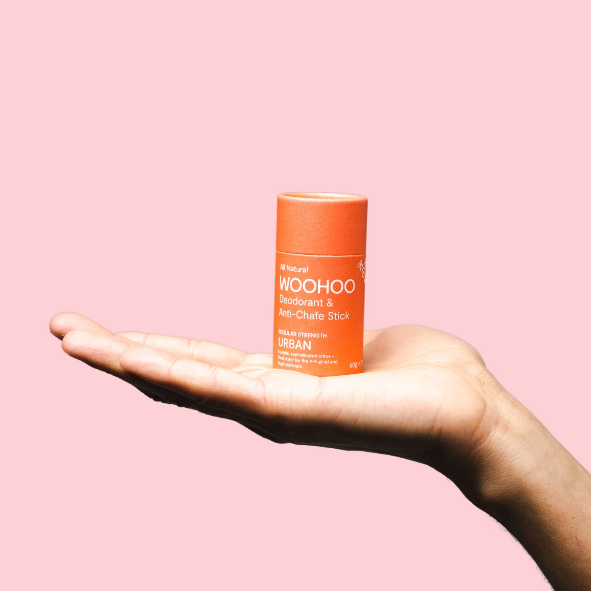 Image of Urban Natural Deodorant Stick sitting on the palm of a hand with a pink background